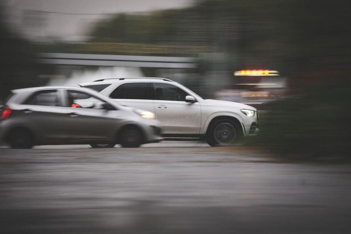 Two cars traveling side by side on a wet, blurred roadway