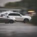 Two cars traveling side by side on a wet, blurred roadway