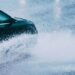 Dark car splashing through heavy rain, with water obscuring its front