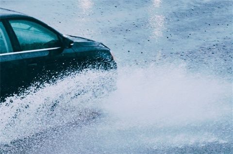 Dark car splashing through heavy rain, with water obscuring its front